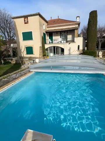 Piscine bleue sous abri télescopique devant une maison provençale